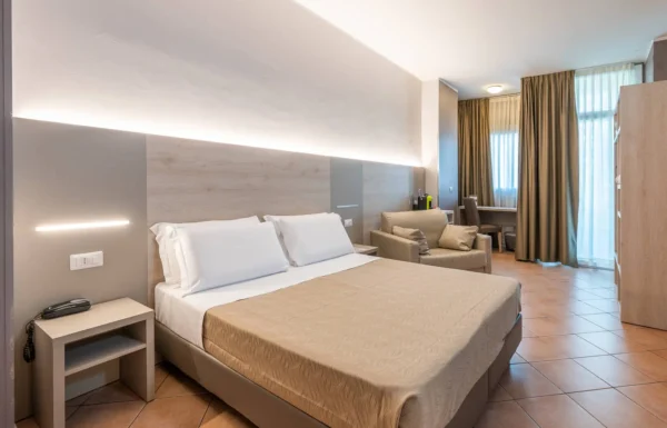 Camera d'albergo luminosa con letto matrimoniale e poltrona.