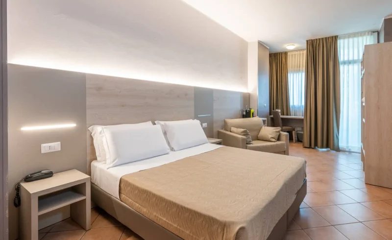Camera d'albergo luminosa con letto matrimoniale e poltrona.