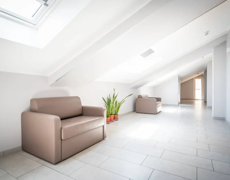 Corridoio luminoso con poltrone beige e pianta verde.